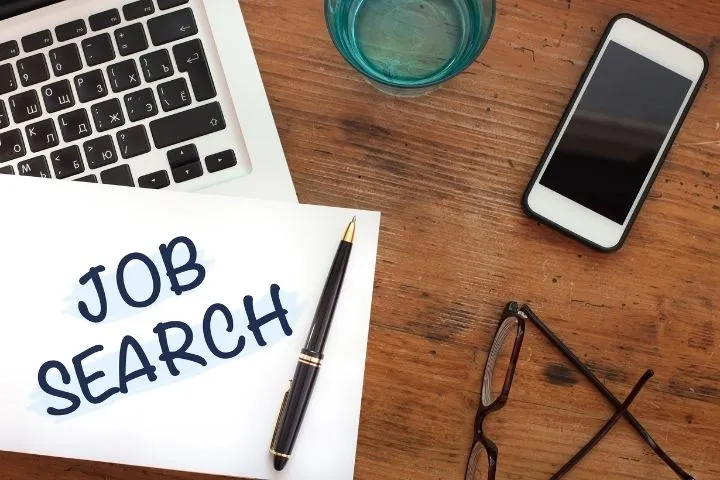 JOB SEARCHと書かれた紙とスマートフォンとパソコンと眼鏡の画像