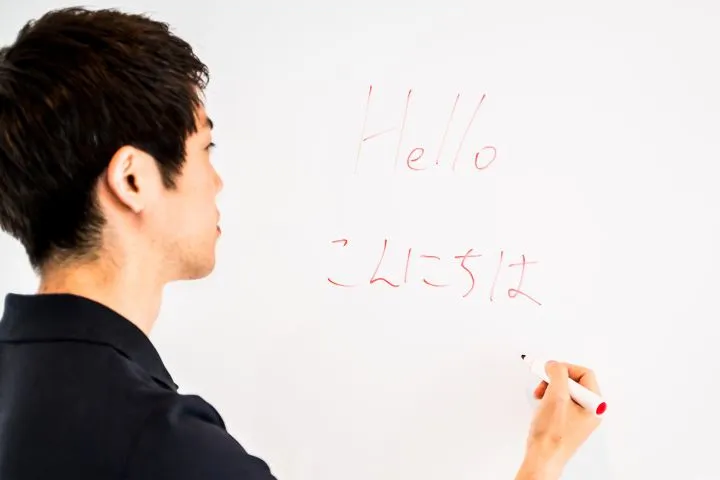 ホワイトボードに英語と日本語を書いている男性の画像