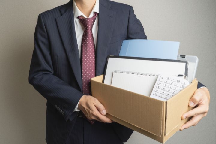 リストラされたビジネスマンが自分の荷物を抱えている画像
