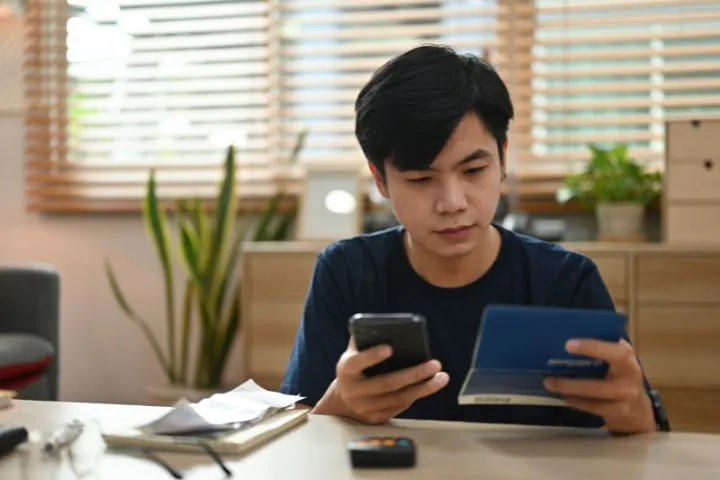 通帳を見ながらスマホを操作する男性
