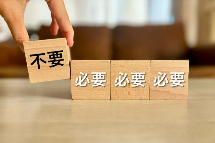 不要と書かれたブロックを持つ手と必要と書かれたブロックの画像