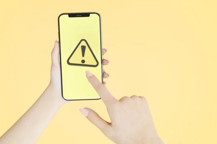 スマホ画面に注意マークが表示されているイメージ