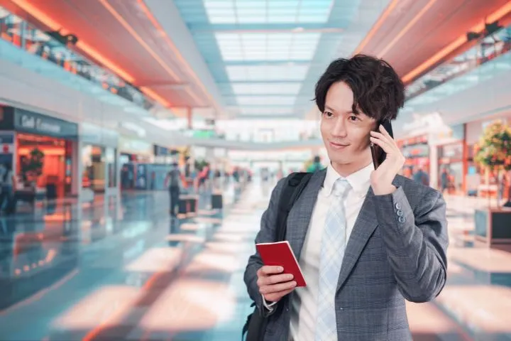 パスポートを持って電話を耳に当てているビジネスマンの」イメージ