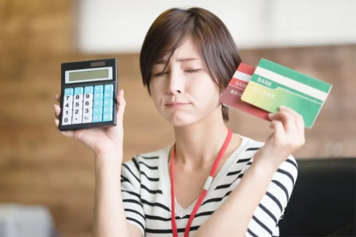 通帳と電卓を手に悩んでいる様子の女性