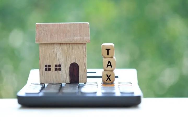 電卓の上に家の模型とTAXと書かれた積木が置かれている様子