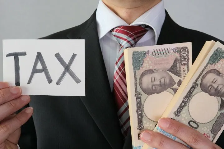 スーツ姿の男性が紙幣とTAXと書かれた紙を持っている様子