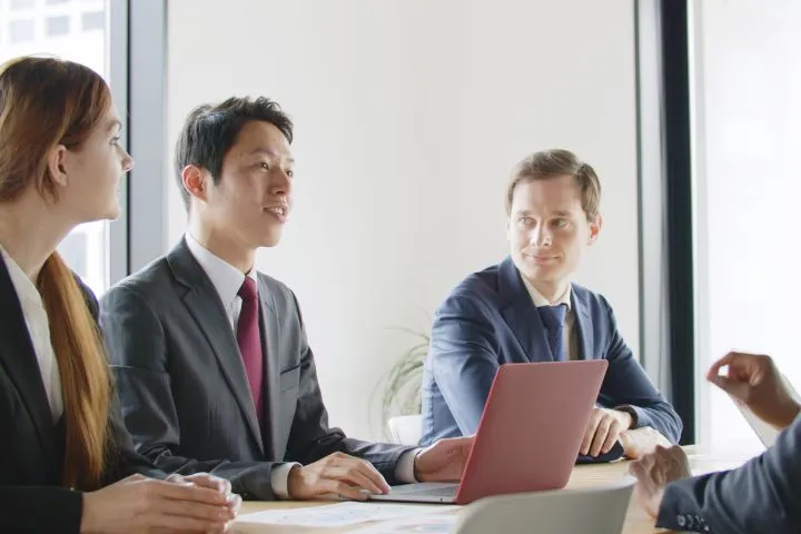 外国人に囲まれて会話をするビジネスマンのイメージ