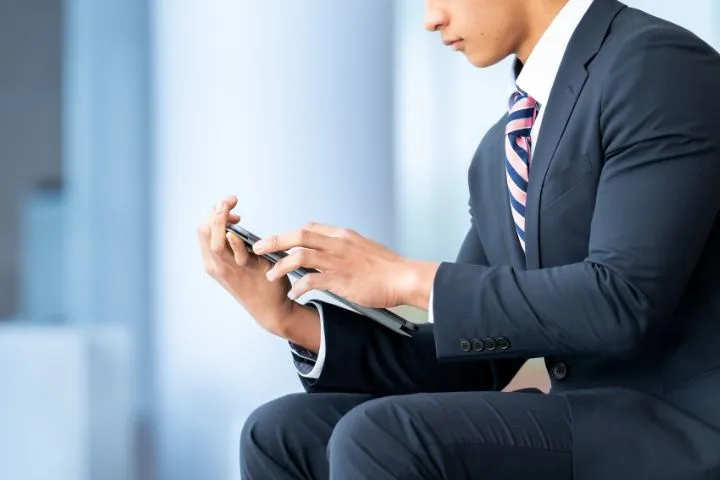 スーツの若い男性がスマートフォンを操作している画像