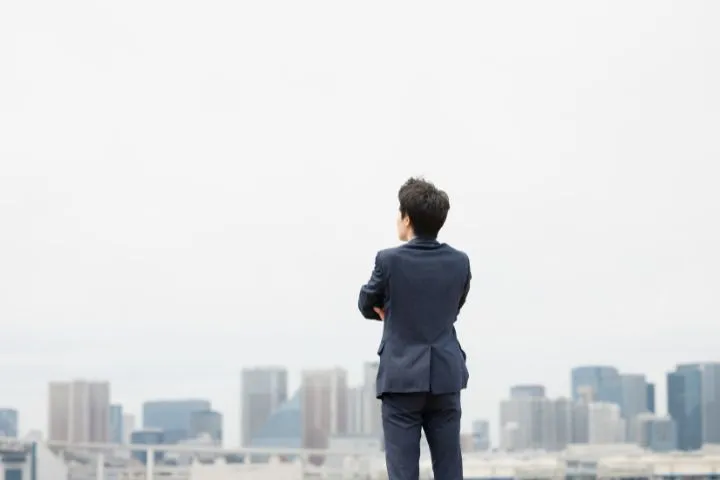 オフィスを眺めるスーツ姿の若い男性の画像