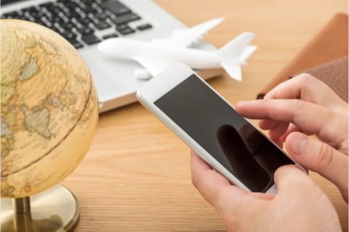 スマホを持つ人の手とパソコンと飛行機と地球儀の画像