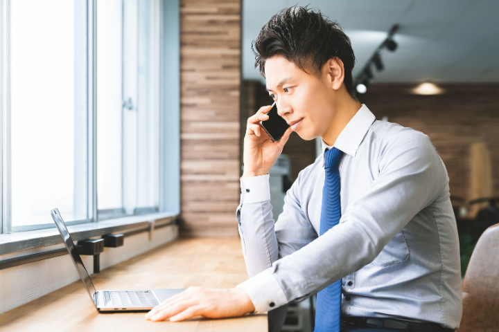 カフェでスマホとPCを使い作業する日本人男性のイメージ