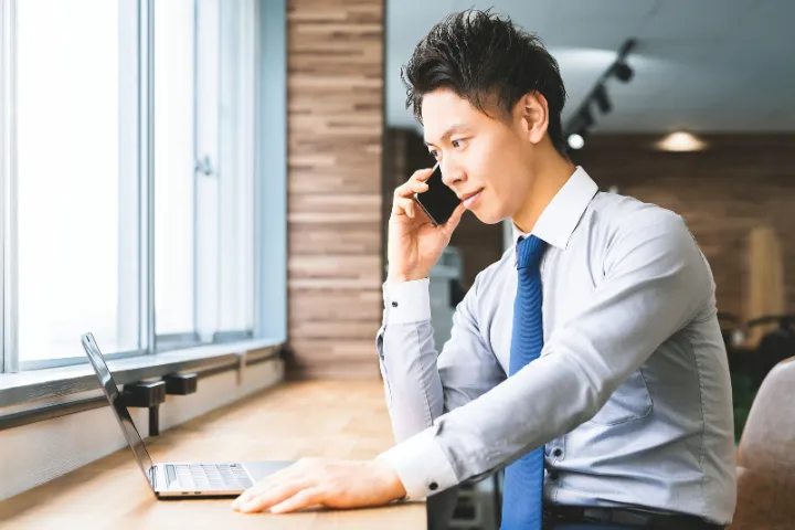 カフェでスマホとPCを使い作業する日本人男性のイメージ