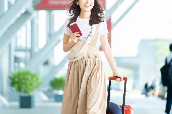 空港でパスポートとキャリーケースを持ち笑顔の女性の画像