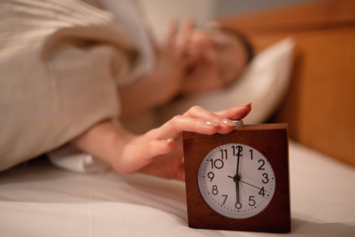6時を差す目覚まし時計をあくびをしながら止める女性の画像