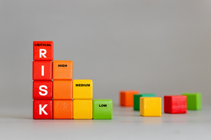 RISKと書かれた赤い積木が積み重なってその横にオレンジ、黄色、黄緑の積木が一段ずつ低く並べられている画像