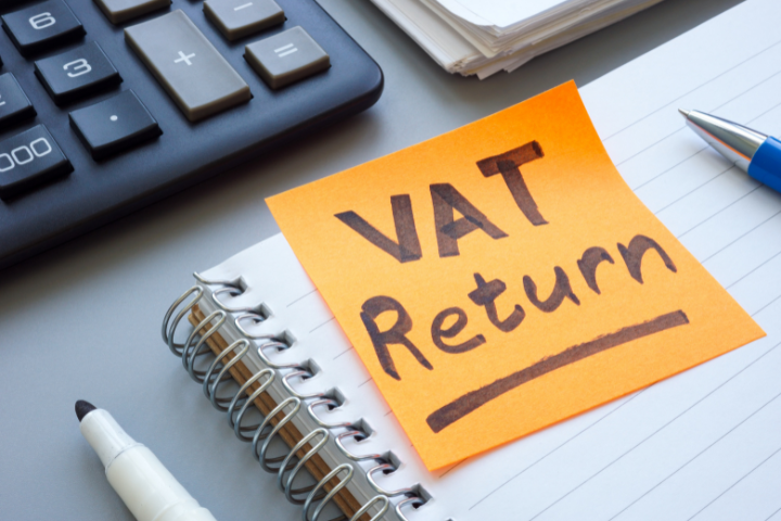 電卓やノートが置かれたデスクにVAT Returnと書かれた付箋がある画像