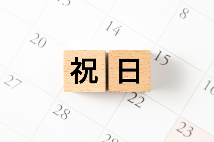 カレンダーの上に祝日と書かれた木のブロックが置いてあるイメージ