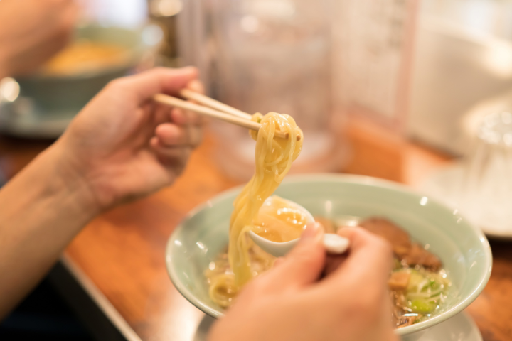 蓮華を持ち箸でラーメンを取っている人の画像