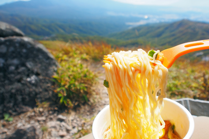 山頂でカップラーメンをフォークで食べようとしている画像