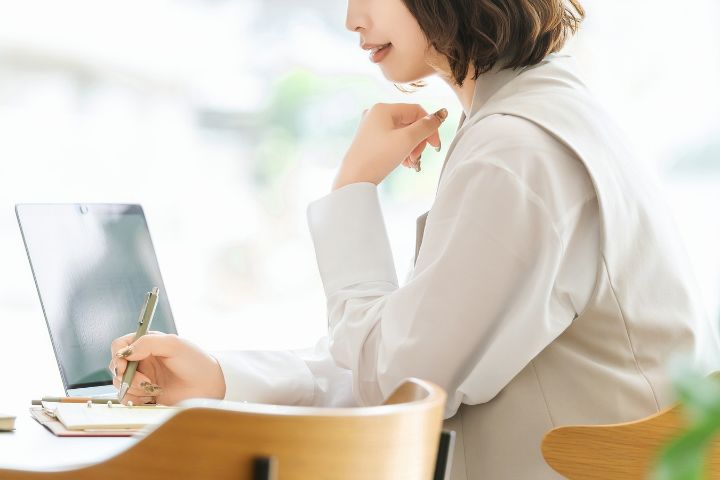 ノートパソコンを開きメモを取っている女性の画像