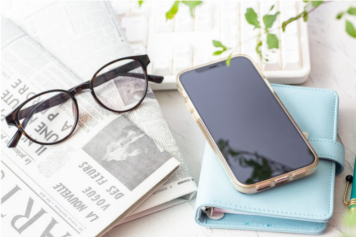 眼鏡とスマホと手帳と英字新聞の画像