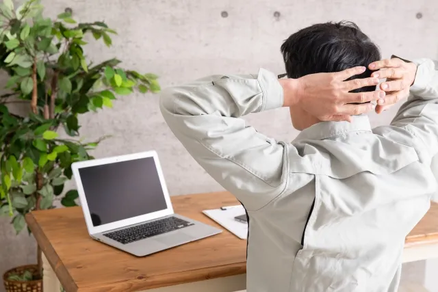 ノートを前に両手を後頭部に当てている男性の画像