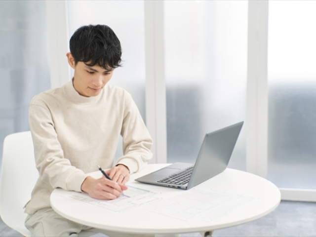 パソコンの前でメモを取る若い男性の画像