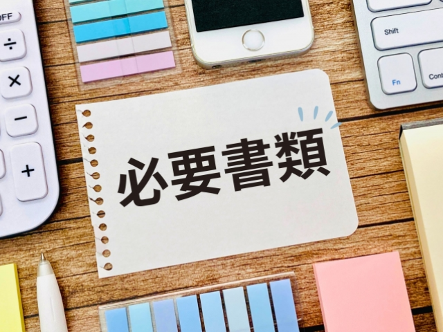 必要書類と書かれた紙を中心に周りに電卓やメモが置かれている画像
