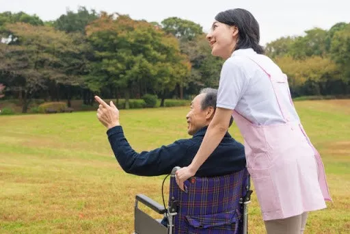 男性が乗っている車椅子を押しながら外を散歩している女性介護士のイメージ