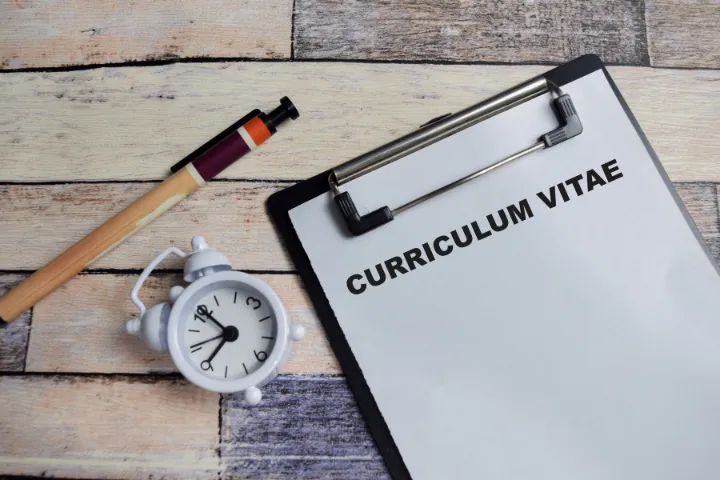 Curriculum Vitaeと書かれた紙がはさんであるバインダーと時計とペンの画像