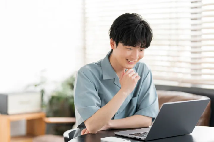 若い男性がノートパソコンを見て考えているイメージ