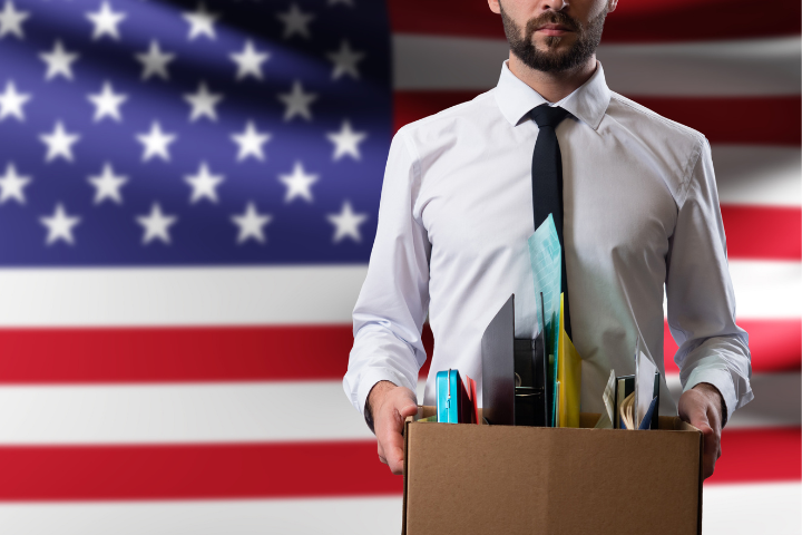 アメリカ国旗をバックに段ボールに入ったデスク用品を持つ男性の画像