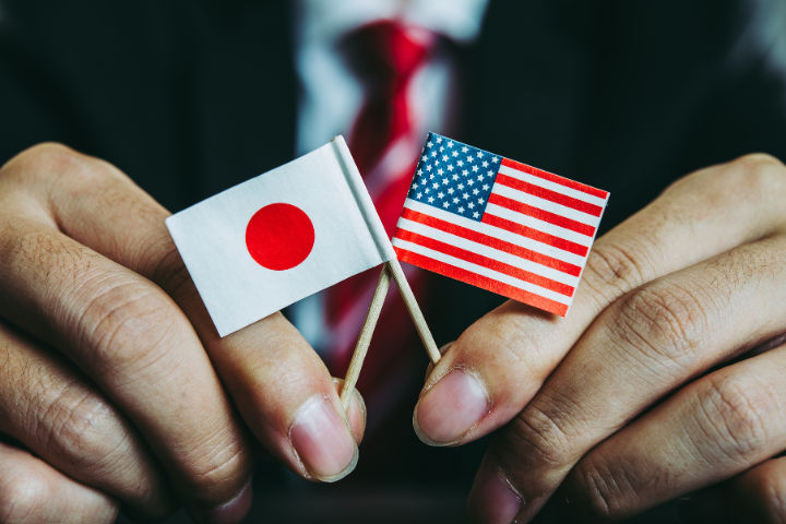 ビジネスマンが日本とアメリカのミニチュア国旗を持つ手元の画像