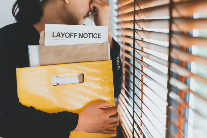 layoff noticeと書かれた書類を持ち涙ぐむ女性の画像