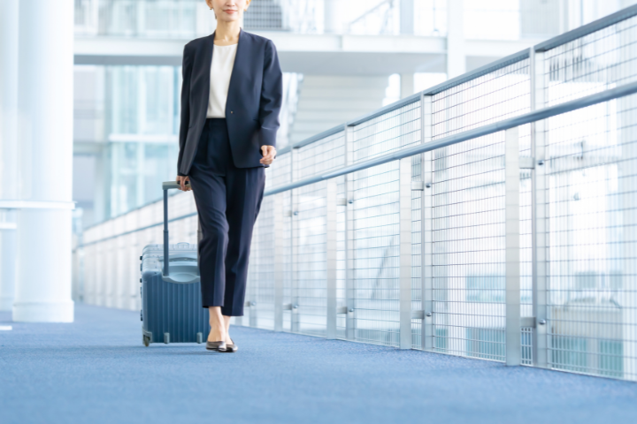 空港でキャリーケースを持って移動するスーツ姿の日本人女性の画像