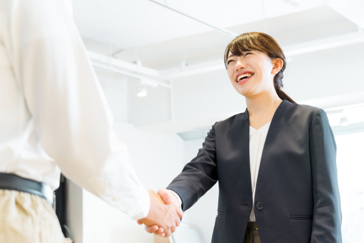 笑顔で握手をするするスーツ姿の若い日本人女性の画像
