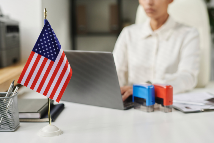 アメリカ国旗が掲げられたオフィスで、従業員がノートパソコンで作業している画像