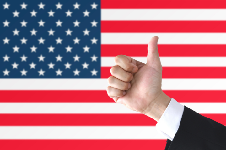 アメリカの国旗の前でサムズアップする男性