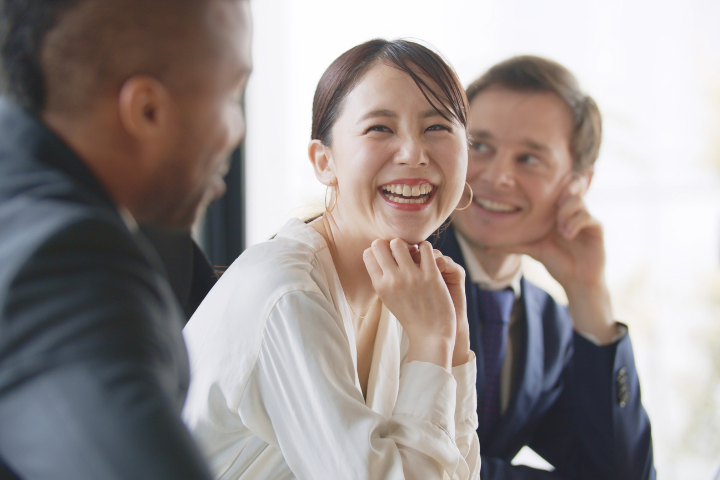 オフィスでスーツ姿の外国人男性と笑顔で会話する日本人女性の画像